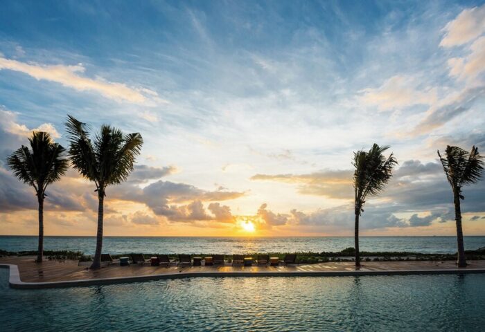 Sunset view from the pool at Andaz Mayakoba Resort Riviera Maya, a gay-friendly hotel by Hyatt. Palm trees and ocean create a relaxing vibe.