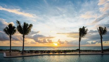 Sunset view from the pool at Andaz Mayakoba Resort Riviera Maya, a gay-friendly hotel by Hyatt. Palm trees and ocean create a relaxing vibe.
