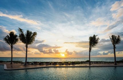Sunset view from the pool at Andaz Mayakoba Resort Riviera Maya, a gay-friendly hotel by Hyatt. Palm trees and ocean create a relaxing vibe.