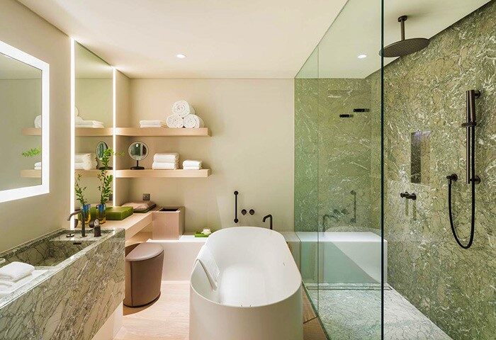 Andaz Seoul Gangnam gay-friendly hotel bathroom. Features a soaking tub, marble sink, shelving with towels, and a glass-enclosed shower.