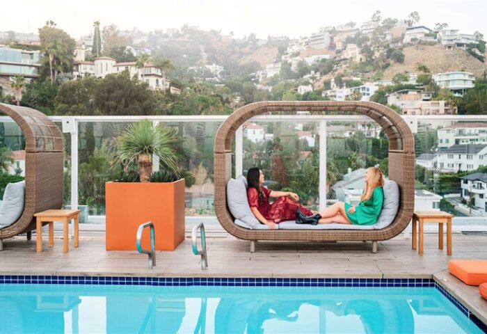 Andaz West Hollywood gay-friendly hotel pool view. Two women lounge on a stylish poolside daybed with city views. Luxury travel for gay men.