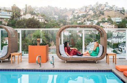 Andaz West Hollywood gay-friendly hotel pool view. Two women lounge on a stylish poolside daybed with city views. Luxury travel for gay men.
