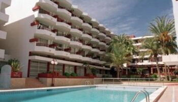 Apartamentos Lido, a gay-friendly hotel. Features a swimming pool, palm trees, and white buildings with red accents. Ideal for gay travel.