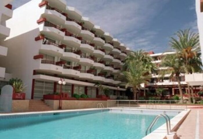 Apartamentos Lido, a gay-friendly hotel. Features a swimming pool, palm trees, and white buildings with red accents. Ideal for gay travel.