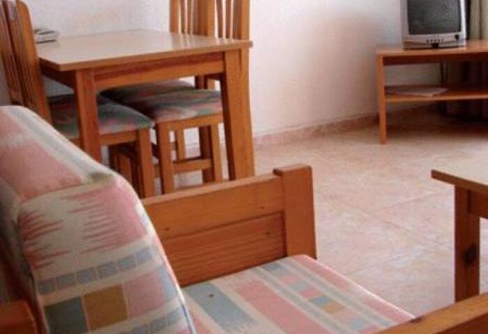 Apartamentos Lido gay-friendly hotel room. Interior of a room with a table, chairs, TV, and couch. Gay travel advice.