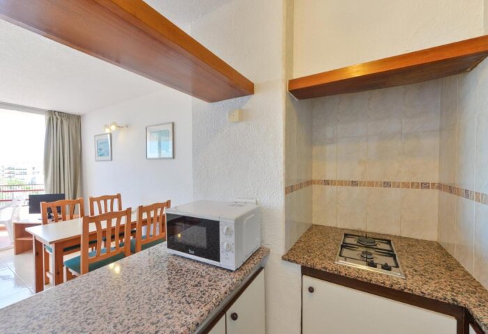 Apartamentos Lido gay-friendly hotel kitchen. Microwave and gas stove on granite countertops. Dining table and balcony visible.