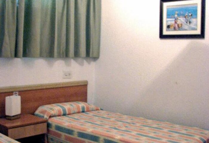 Apartamentos Lido gay-friendly hotel room. Twin beds, bedside table, ceiling fan, and picture on the wall. Gay travel lodging option.