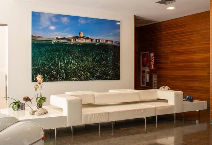 Apartamentos Llobet lobby. Gay-friendly hotel interior with modern white sofa, beach art, and wood paneling. Stylish gay travel lodging.