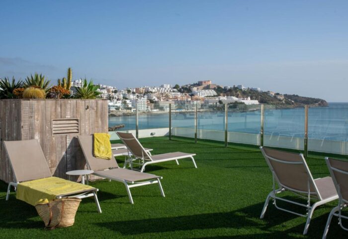 Rooftop view at Gay-Friendly Hotel Apartamentos Llobet. Sun loungers, ocean view, and cityscape. Ideal for gay travel in Ibiza, Spain.