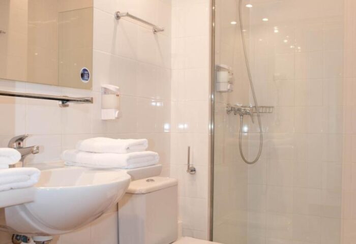 Bathroom at Gay-Friendly Hotel Apartamentos Llobet. Clean, white tiled walls, sink, toilet, and glass shower. Ideal for gay men travelers.