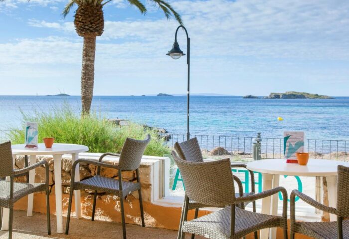 Gay-Friendly Hotel Apartamentos Mar y Playa view. Tables and chairs overlook the sea. Palm tree and islands in the background.