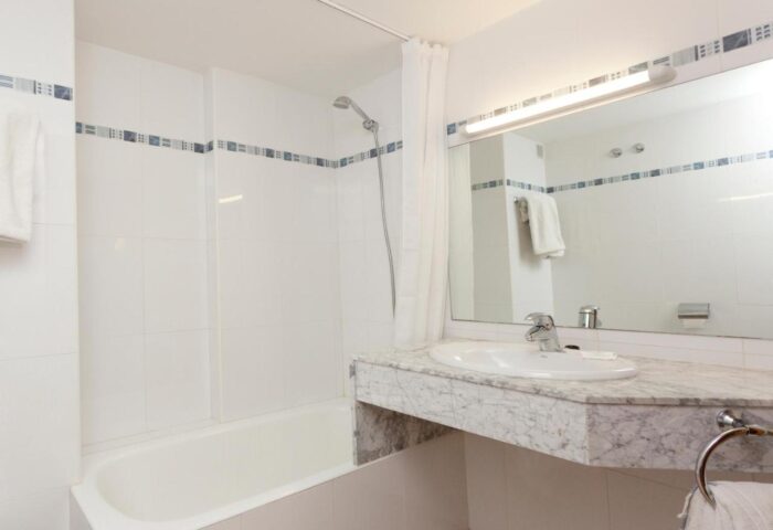Bathroom at Gay-Friendly Hotel Apartamentos Mar y Playa. Features a tub, shower, sink with marble countertop, and large mirror. Clean design.