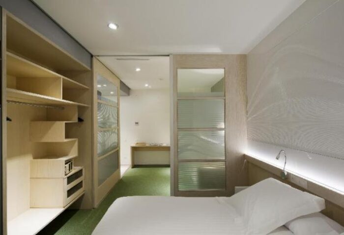 Ako Suites Hotel aparthotel interior. Gay-friendly hotel room with bed, closet, and frosted glass doors. Modern design, sleek and comfortable.