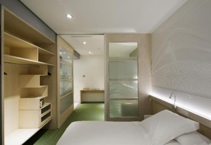 Ako Suites Hotel aparthotel interior. Gay-friendly hotel room with bed, closet, and frosted glass doors. Modern design, sleek and comfortable.