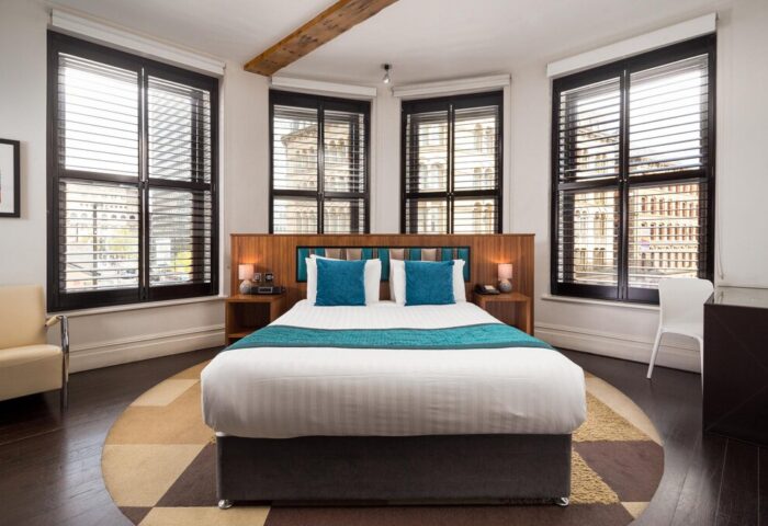 Roomzzz Manchester City aparthotel room. Gay-friendly hotel with double bed, blue cushions, and large windows. Stylish interior for gay travelers.