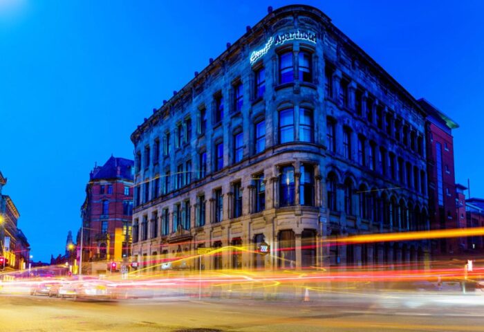 Roomzzz Aparthotel Manchester City at night. Gay-friendly hotel with light trails. Urban scene for gay men travel advice.