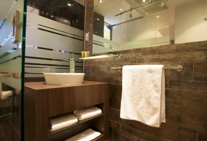 Roomzzz Aparthotel Manchester City bathroom. Modern design with a vessel sink, dark wood cabinets, and a glass-enclosed shower. Gay-friendly hotel.