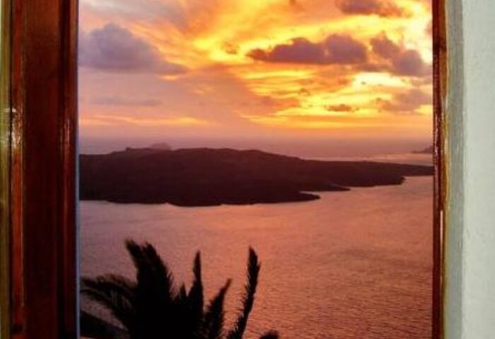 View from Aperto Suites, a gay-friendly, adults-only hotel. Sunset over the sea, seen through a window. Palm tree silhouette. Romantic.