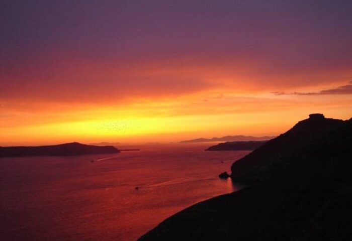 Sunset view from Aperto Suites, an adults-only, gay-friendly hotel. The sky is a mix of purple, orange, and yellow over the sea.
