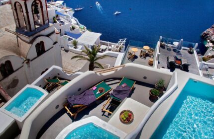 Aperto Suites Adults Only, gay-friendly hotel. View of Santorini's white architecture, Aegean Sea, private pools, and sun loungers.