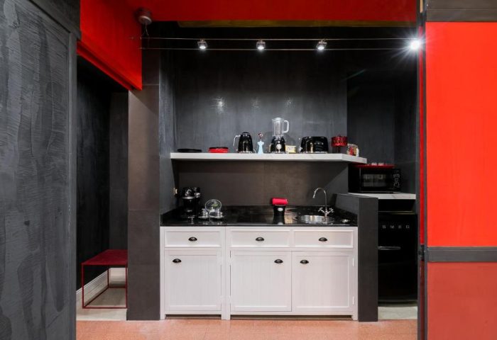 MarcoAurelio49 Appartamenti's gay-friendly hotel kitchenette. White cabinets, black countertop, and SMEG fridge. Red and black accents.