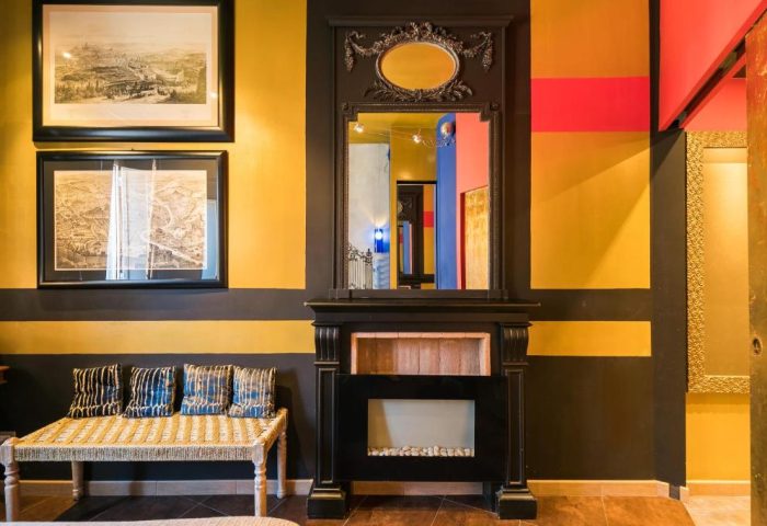 MarcoAurelio49 Apartments' gay-friendly hotel room: Black fireplace with mirror, striped walls, woven bench, and framed art. Unique decor.