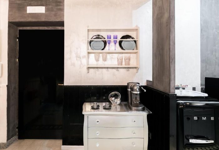MarcoAurelio49 gay-friendly hotel apartment kitchen. Shelves with dishes, glasses, coffee machine, and Smeg refrigerator. Stylish design.