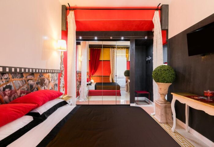 MarcoAurelio49 Apartments' gay-friendly hotel room. Stylish decor, mirrored wall, red accents, and a unique headboard. Comfortable, inviting space.