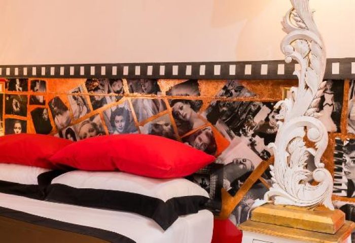 MarcoAurelio49 gay-friendly hotel room. Stylish bedroom with red accents, vintage headboard, and ornate lamp. Gay travel lodging.
