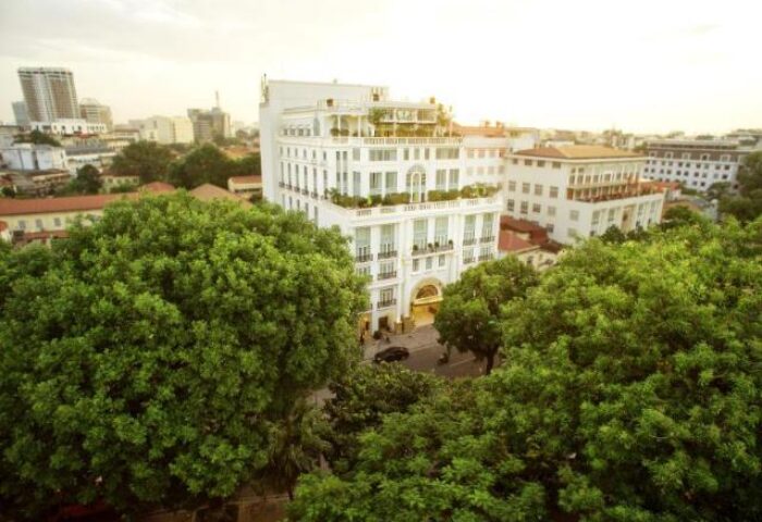 Apricot Hotel, a gay-friendly hotel. Exterior view of the hotel in a cityscape, surrounded by lush greenery. Gay travel lodging.