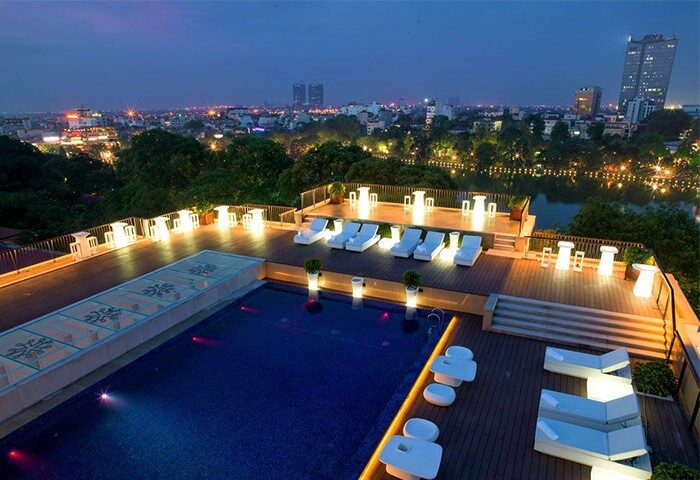 Apricot Hotel's rooftop pool at night. Gay-friendly hotel with city views, lounge chairs, and illuminated tables. Ideal for gay travel.