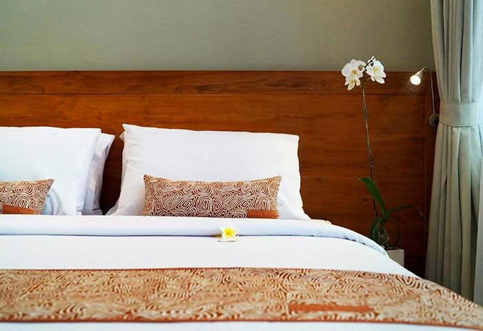 Arana Suite gay-friendly hotel room: Bed with patterned pillows and runner, wooden headboard, orchid, lamp, and curtains. Relaxing travel.