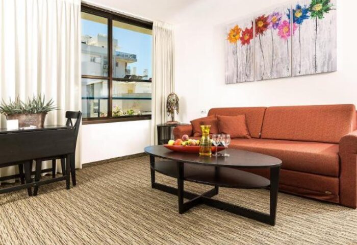 Arbel Suites Hotel room. Gay-friendly hotel suite with couch, table, and colorful flower art. Modern interior design for LGBTQ+ travelers.