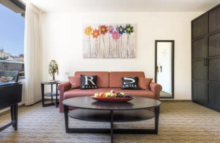 Arbel Suites Hotel gay-friendly suite interior. Living area with sofa, pillows, table, and colorful flower art. Modern design.