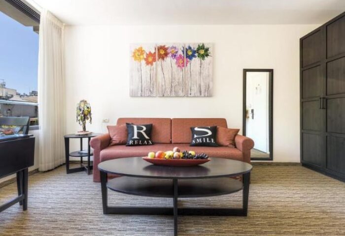 Arbel Suites Hotel gay-friendly suite interior. Living area with sofa, pillows, table, and colorful flower art. Modern design.