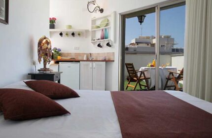 Arbel Suites Hotel room with bed, kitchenette, and balcony. The gay-friendly hotel offers a relaxed stay with outdoor dining. Perfect for gay travel.