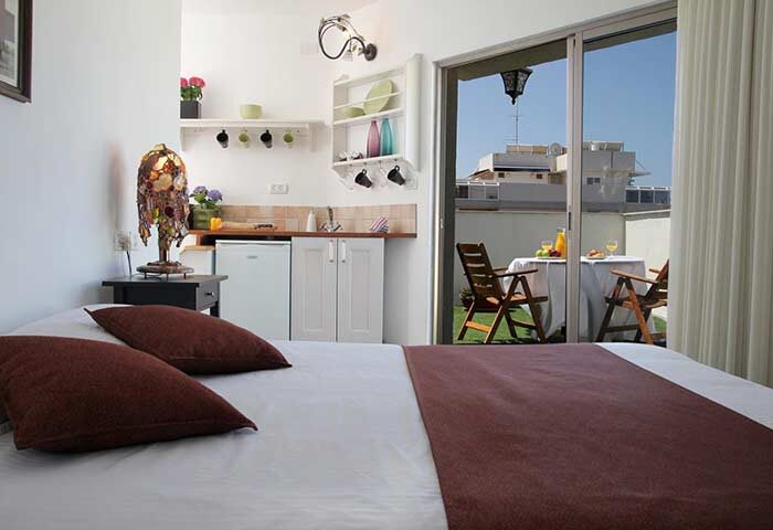 Arbel Suites Hotel room with bed, kitchenette, and balcony. The gay-friendly hotel offers a relaxed stay with outdoor dining. Perfect for gay travel.