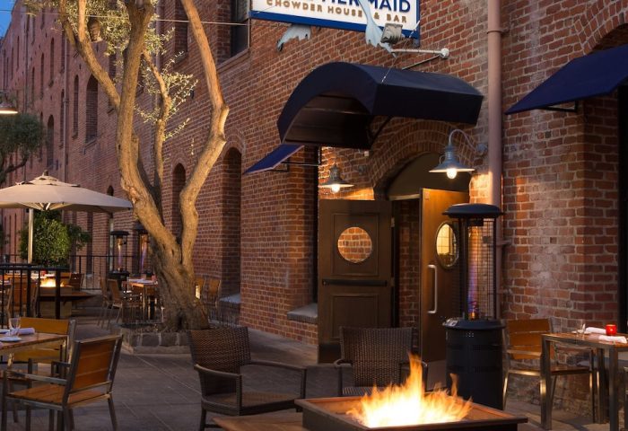 Argonaut Hotel's gay-friendly outdoor patio with a fire pit and tables. The hotel is located in a brick building. It's a great place to relax.