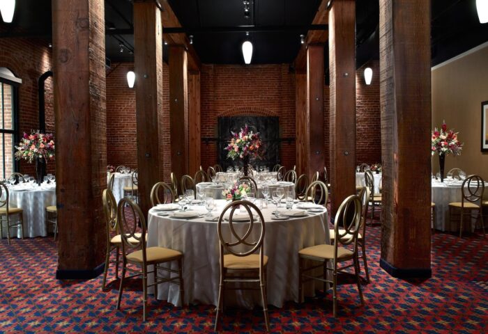 Argonaut Hotel's gay-friendly space. Round tables set for a wedding or event, surrounded by exposed brick and wooden beams. Elegant, historic.