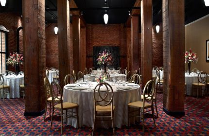 Argonaut Hotel's gay-friendly space. Round tables set for a wedding or event, surrounded by exposed brick and wooden beams. Elegant, historic.