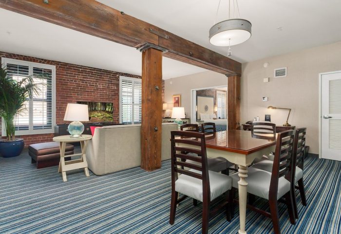 Argonaut Hotel's gay-friendly suite. Living area with brick wall, sofa, and TV. Dining table with chairs. Bedroom view. Stylish, comfortable.