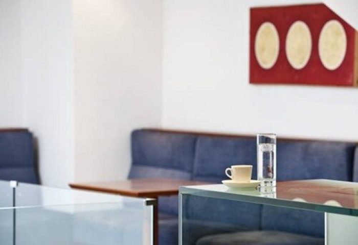 Arion Athens Hotel's gay-friendly ambiance: A glass table with a cup and water, set against a blue sofa and modern art.