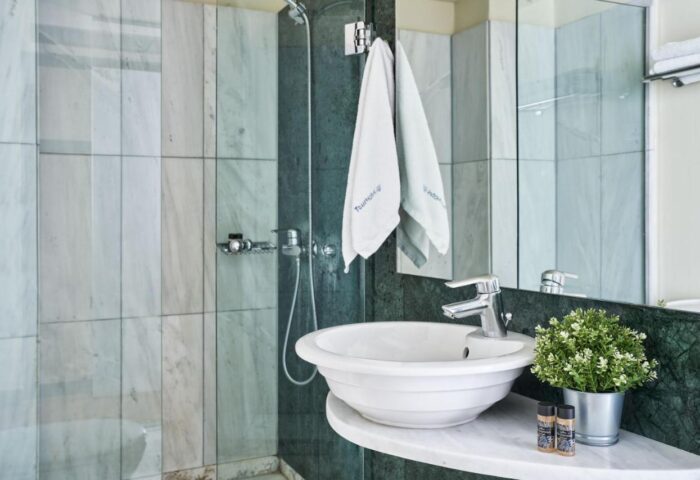 Arion Athens Hotel gay-friendly bathroom. Sink, shower, towels, and plant detail. Gay travel accommodations in Athens.