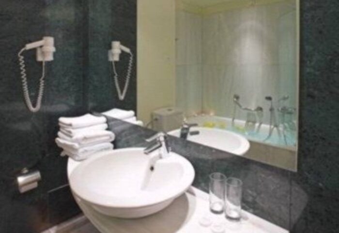 Bathroom at Arion Athens Hotel, a gay-friendly hotel. Sink, towels, hair dryers, and bathtub visible in the mirror. Athens gay travel.