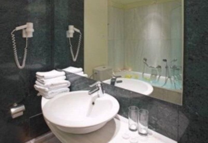 Bathroom at Arion Athens Hotel, a gay-friendly hotel. Sink, towels, hair dryers, and bathtub visible in the mirror. Athens gay travel.