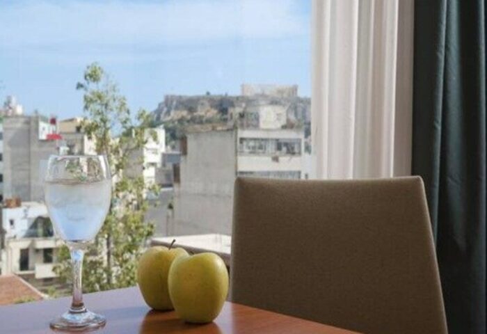 View from Arion Athens Hotel, a gay-friendly hotel. Glass of water and apples on a table. The Acropolis is visible in the background.