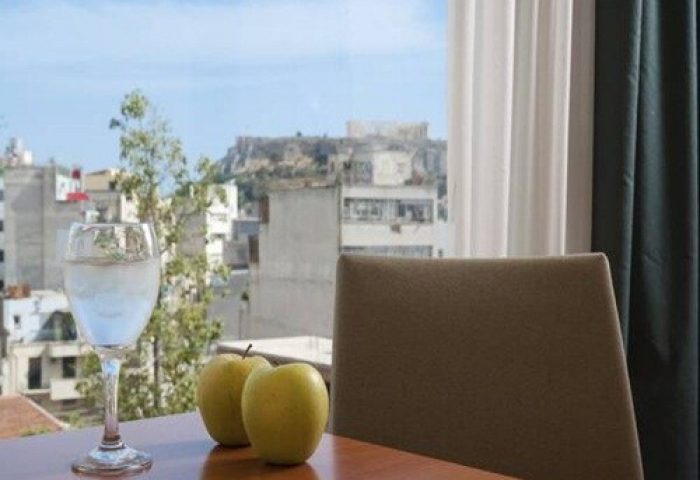 View from Arion Athens Hotel, a gay-friendly hotel. Glass of water and apples on a table. The Acropolis is visible in the background.