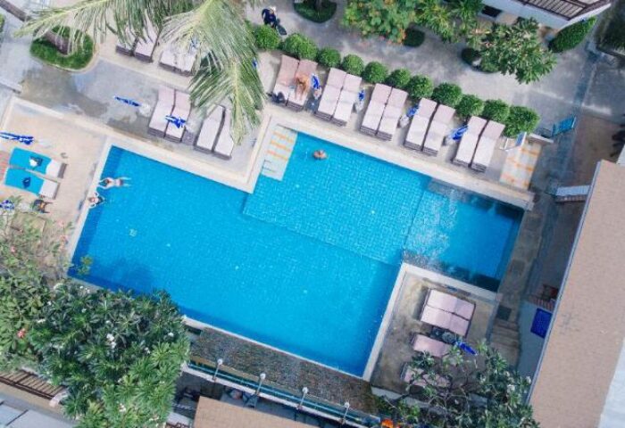 Aerial view of Ark Bar Beach Resort's pool, a gay-friendly hotel. People swim and sunbathe. Lush greenery surrounds the pool area.