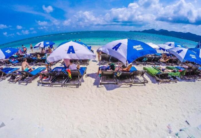 Ark Bar Beach Resort: Sandy beach scene with sunbathers under blue umbrellas. Gay-friendly hotel for a relaxing vacation.