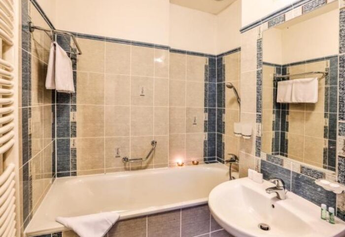 Bathroom interior at Arkada Hotel Praha, a gay-friendly hotel. Features a bathtub, sink, and tiled walls. Ideal accommodation for gay travelers.